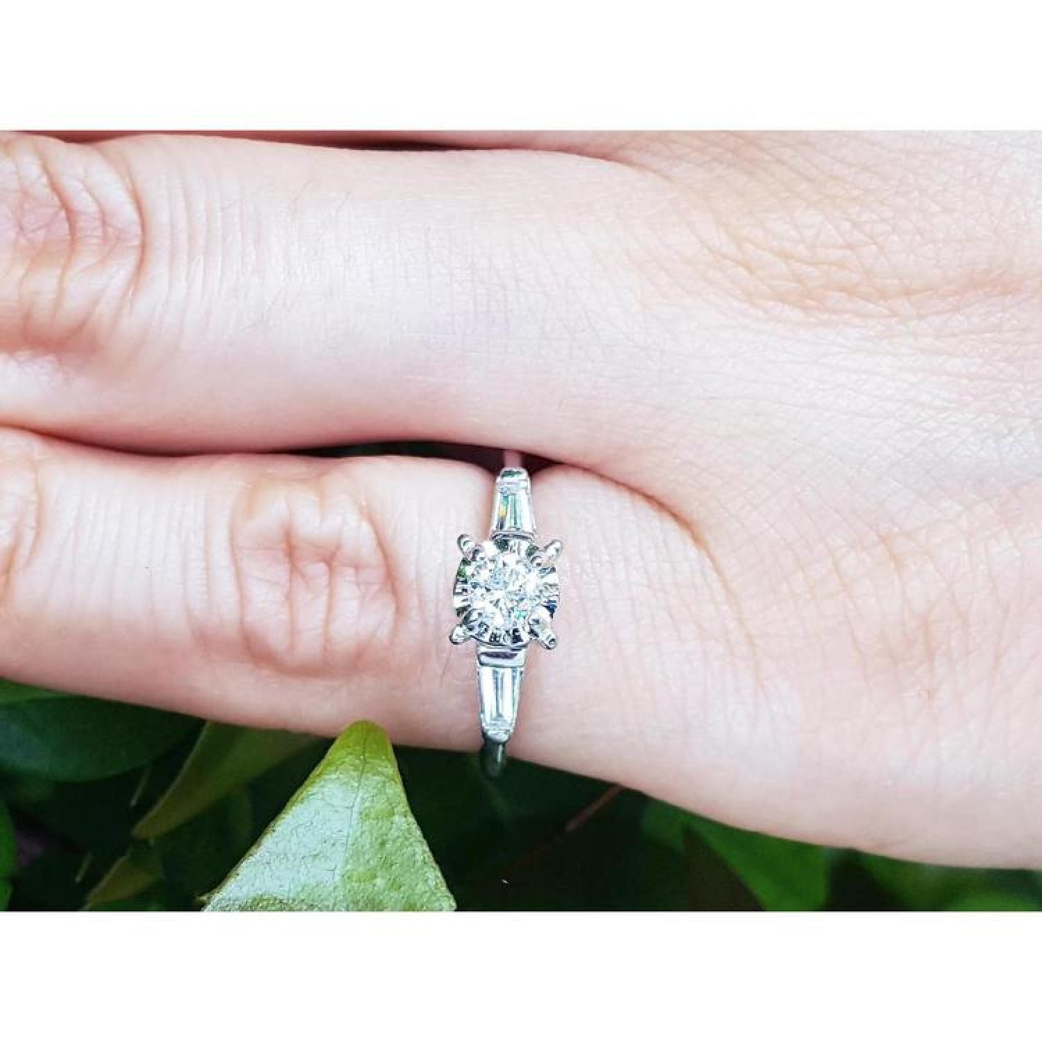 14k white gold engagement ring with round diamond and baguette side stones on a finger.