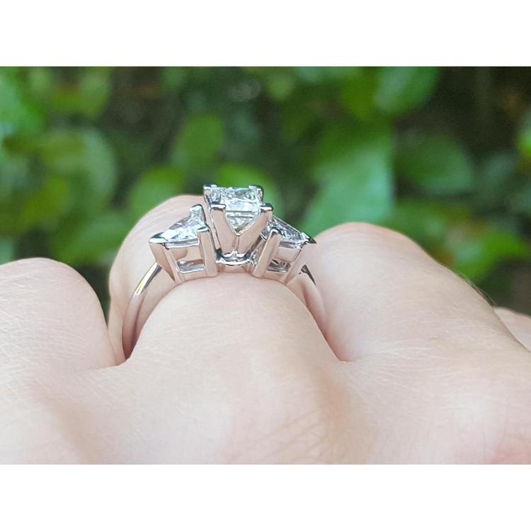 14K white gold ring with a princess cut diamond center and trillion side diamonds, worn on a finger.