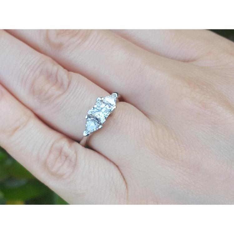 14K white gold ring with a princess cut diamond flanked by two trillion side diamonds on a hand.
