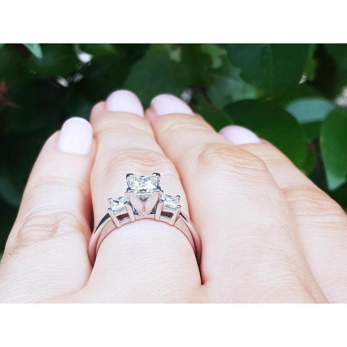 White gold 14K three-stone princess cut diamond ring on a hand, featuring a large center diamond.