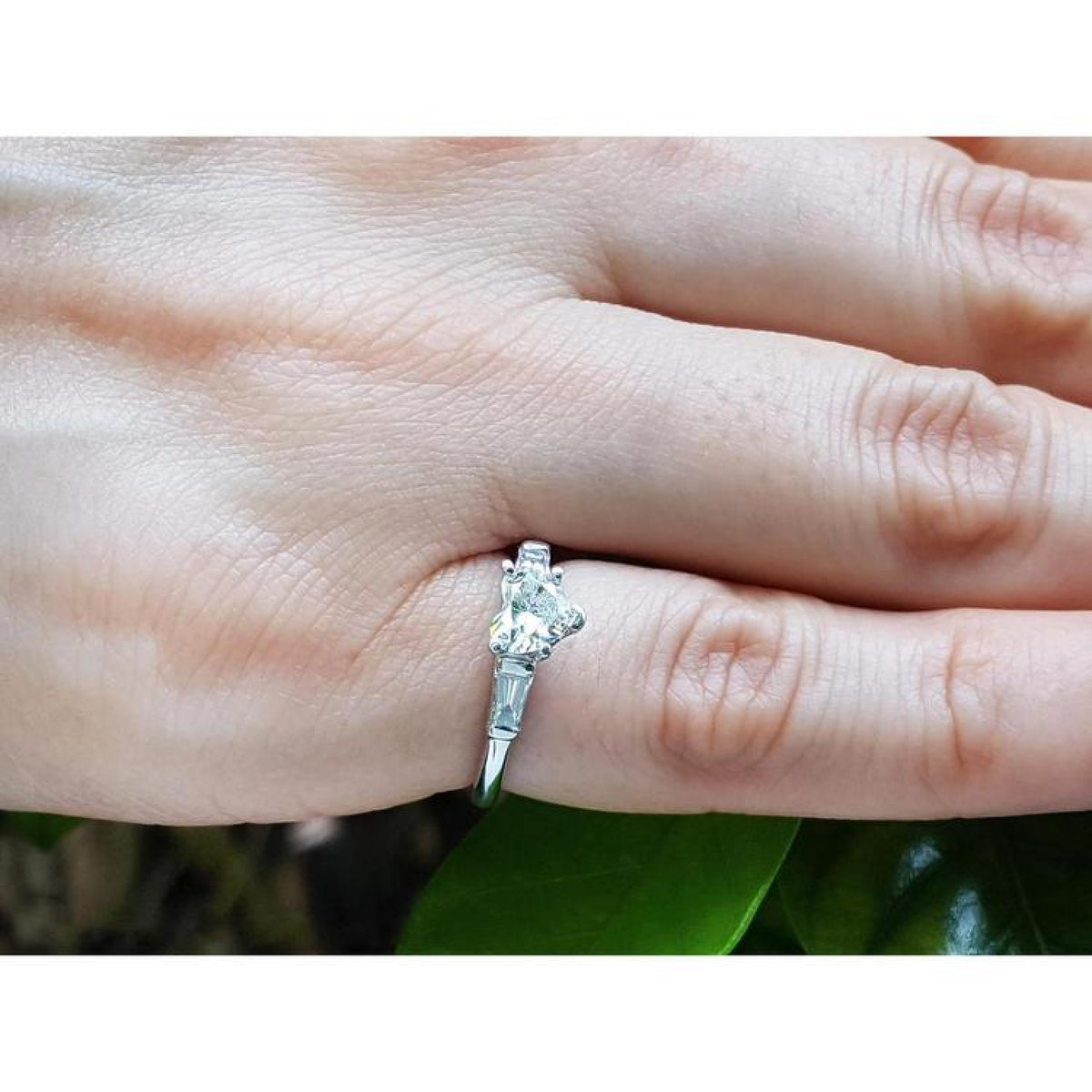 Heart-cut diamond engagement ring with side baguette diamonds in 14K white gold on a finger.