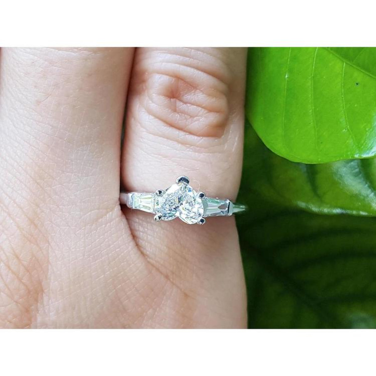 14K white gold heart cut diamond ring with side tapered baguette diamonds on a finger.