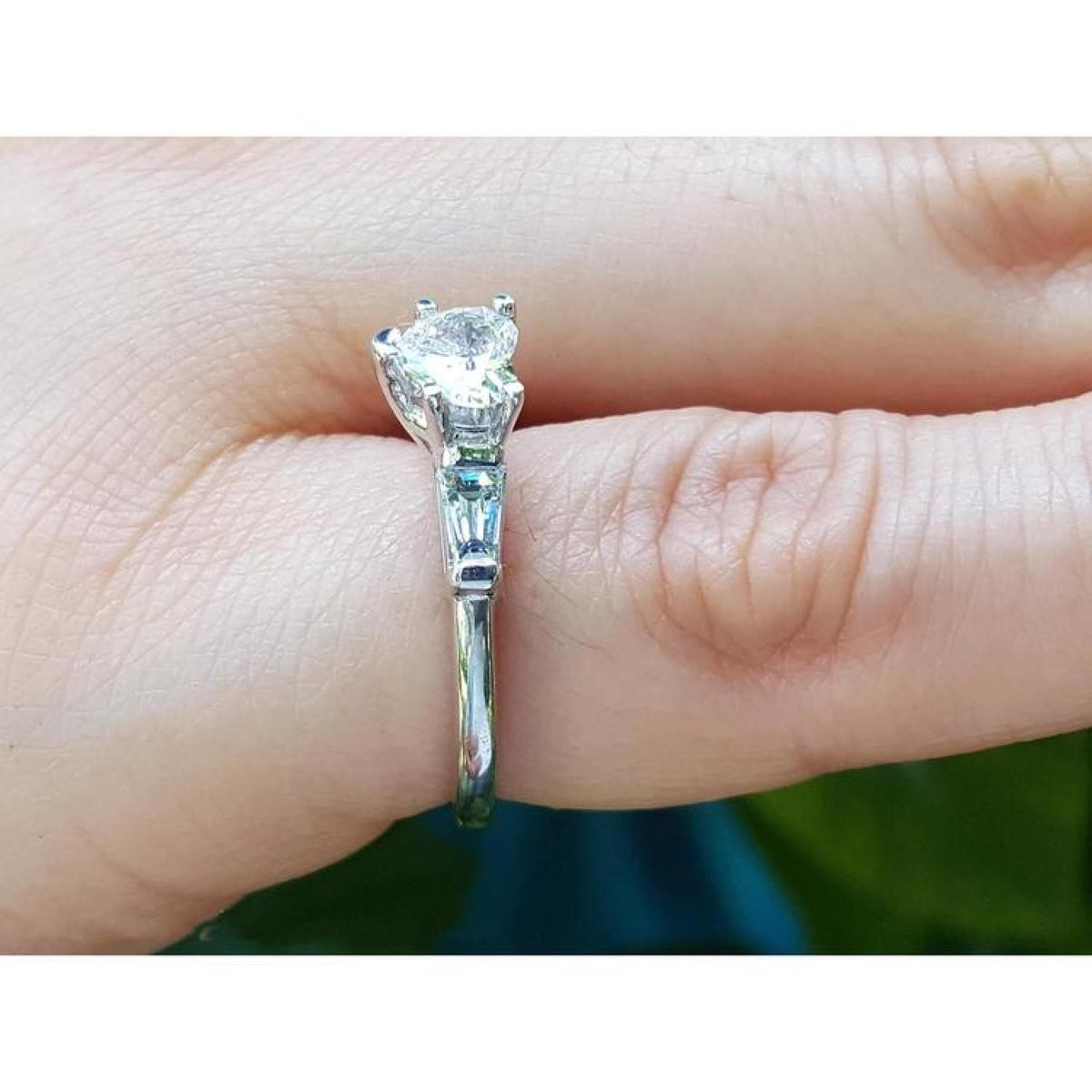 14K white gold ring with a heart-cut diamond center stone and side baguette diamonds on a finger.