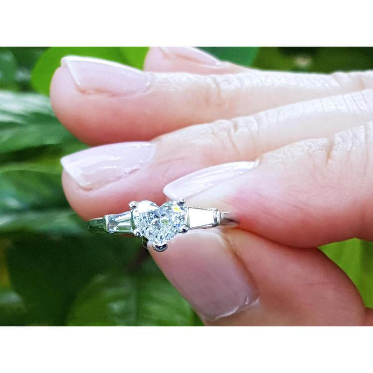 Heart-cut diamond ring with side baguette diamonds in 14K white gold, held by fingers.