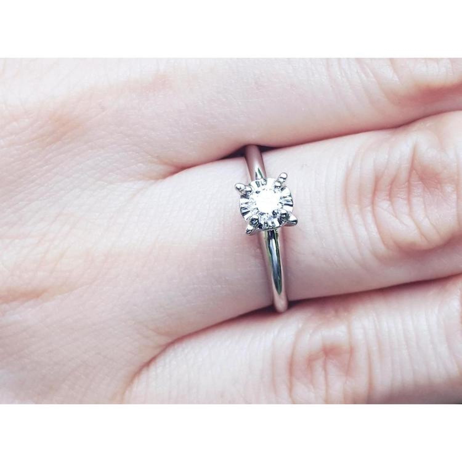 Round cut diamond solitaire engagement ring in 14K white gold, worn on a finger.