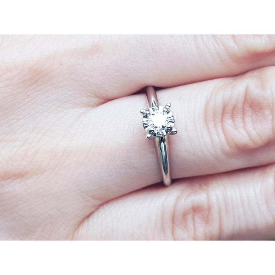 Round cut diamond solitaire engagement ring in 14K white gold, worn on a finger.