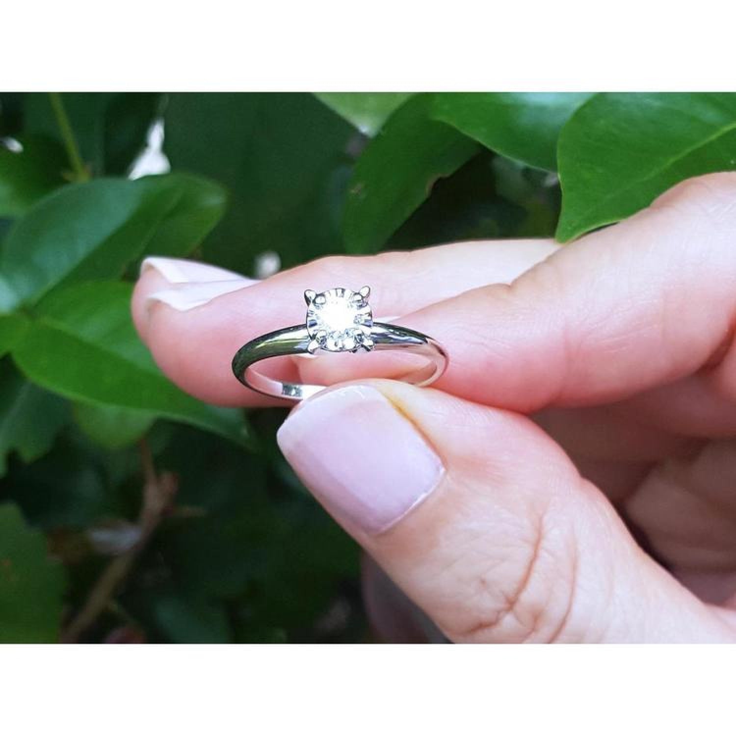 Hand holding a round cut diamond solitaire engagement ring in 14K white gold with an illusion setting.