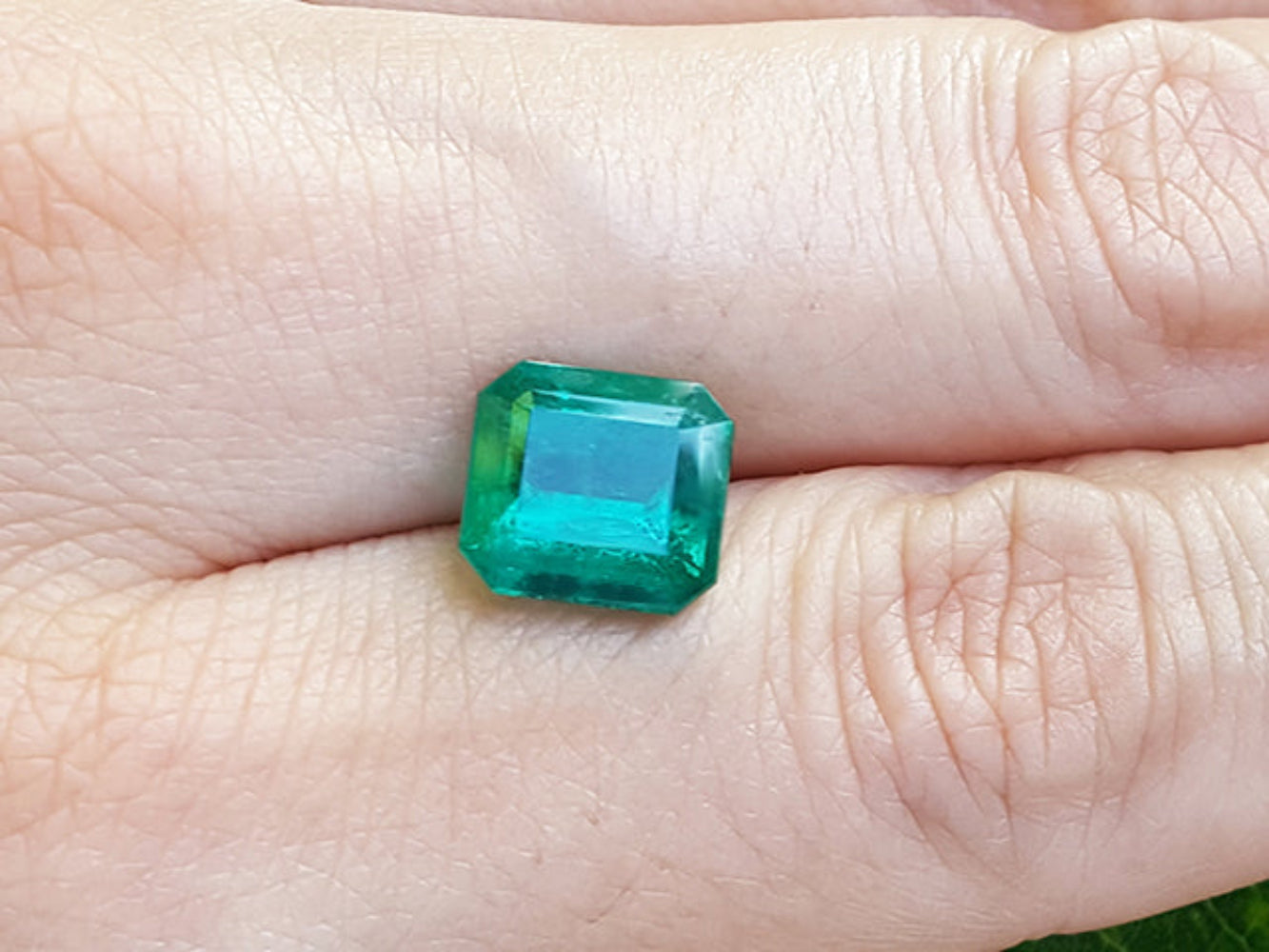 A GIA certified F1 natural colombian loose emerald held between fingers