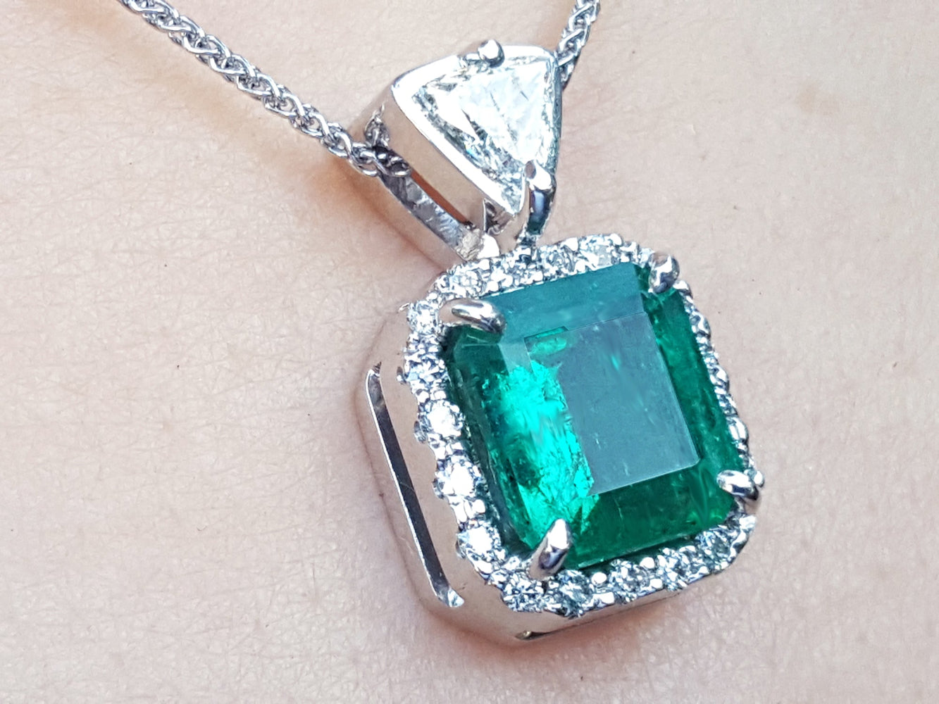 A natural certified emerald pendant with gold chain on a light background