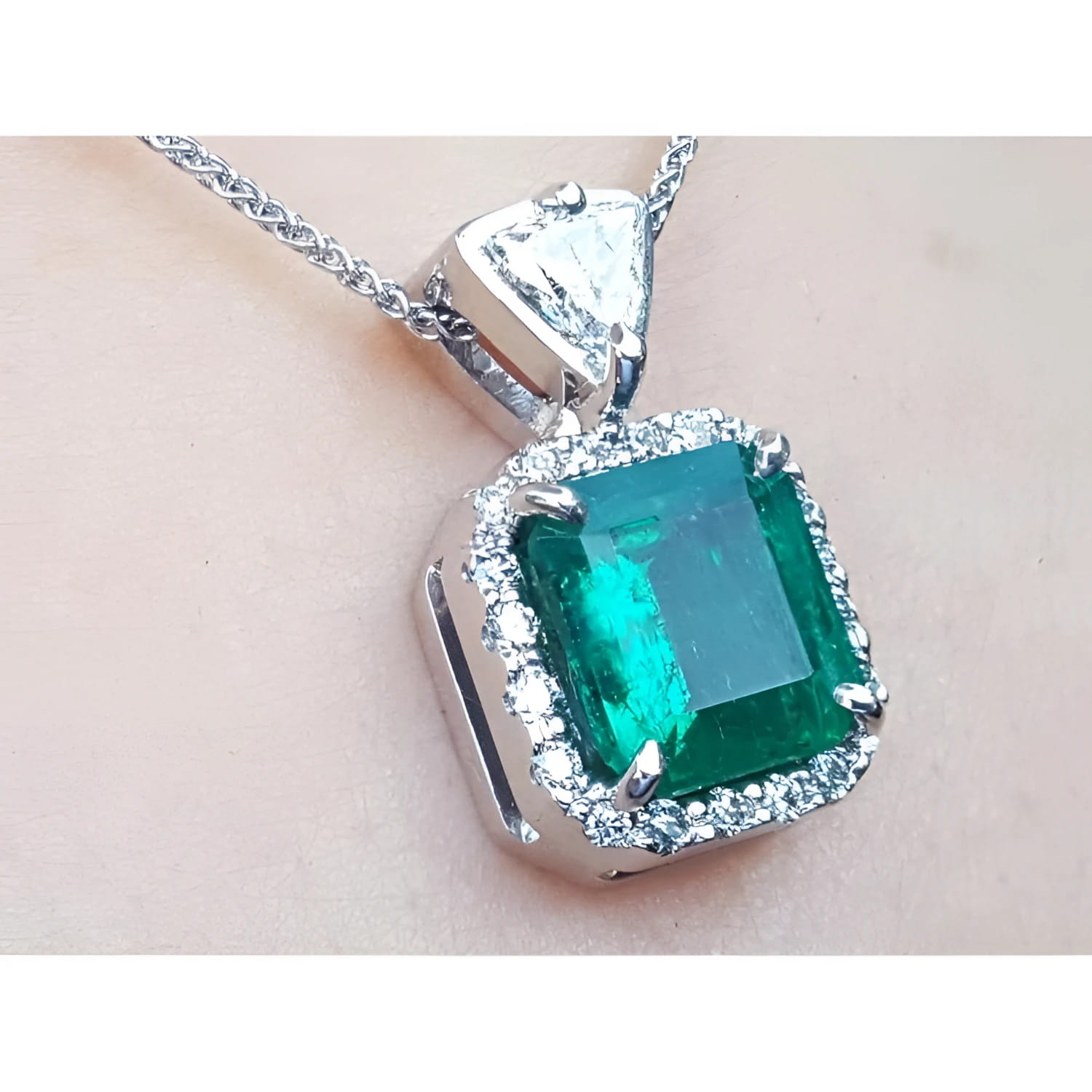 A natural certified emerald pendant with gold chain on a light background