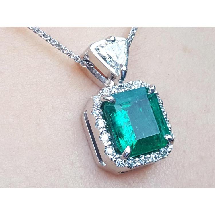 A natural certified emerald pendant with gold chain on a light background