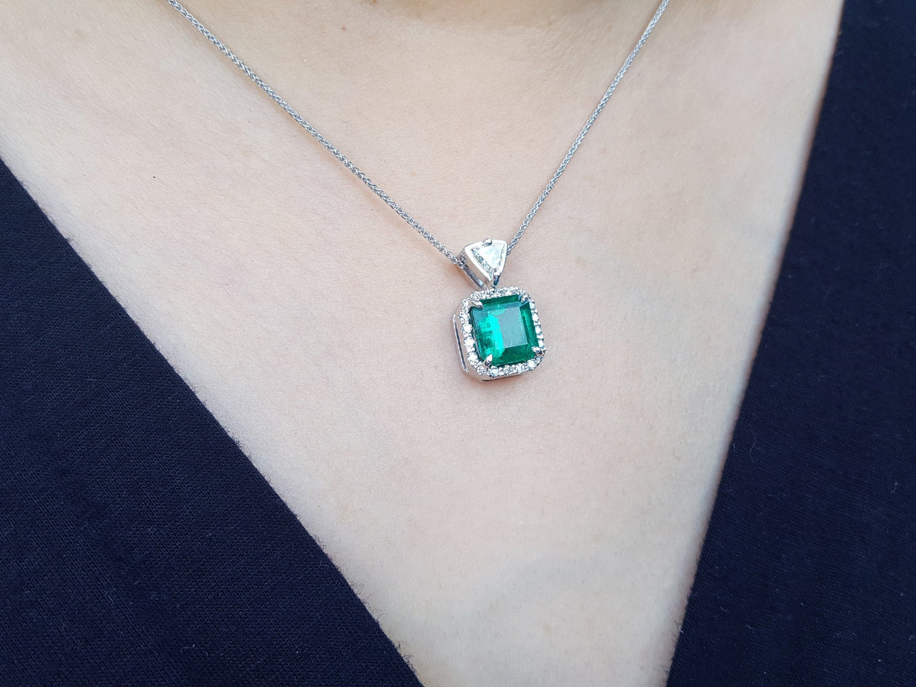 Emerald green gemstone necklace on a person wearing a dark blue top.