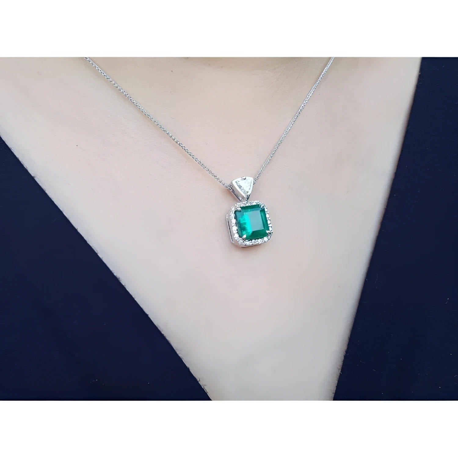 Colombian emerald pendant in 18K white gold with diamond halo on a silver chain.