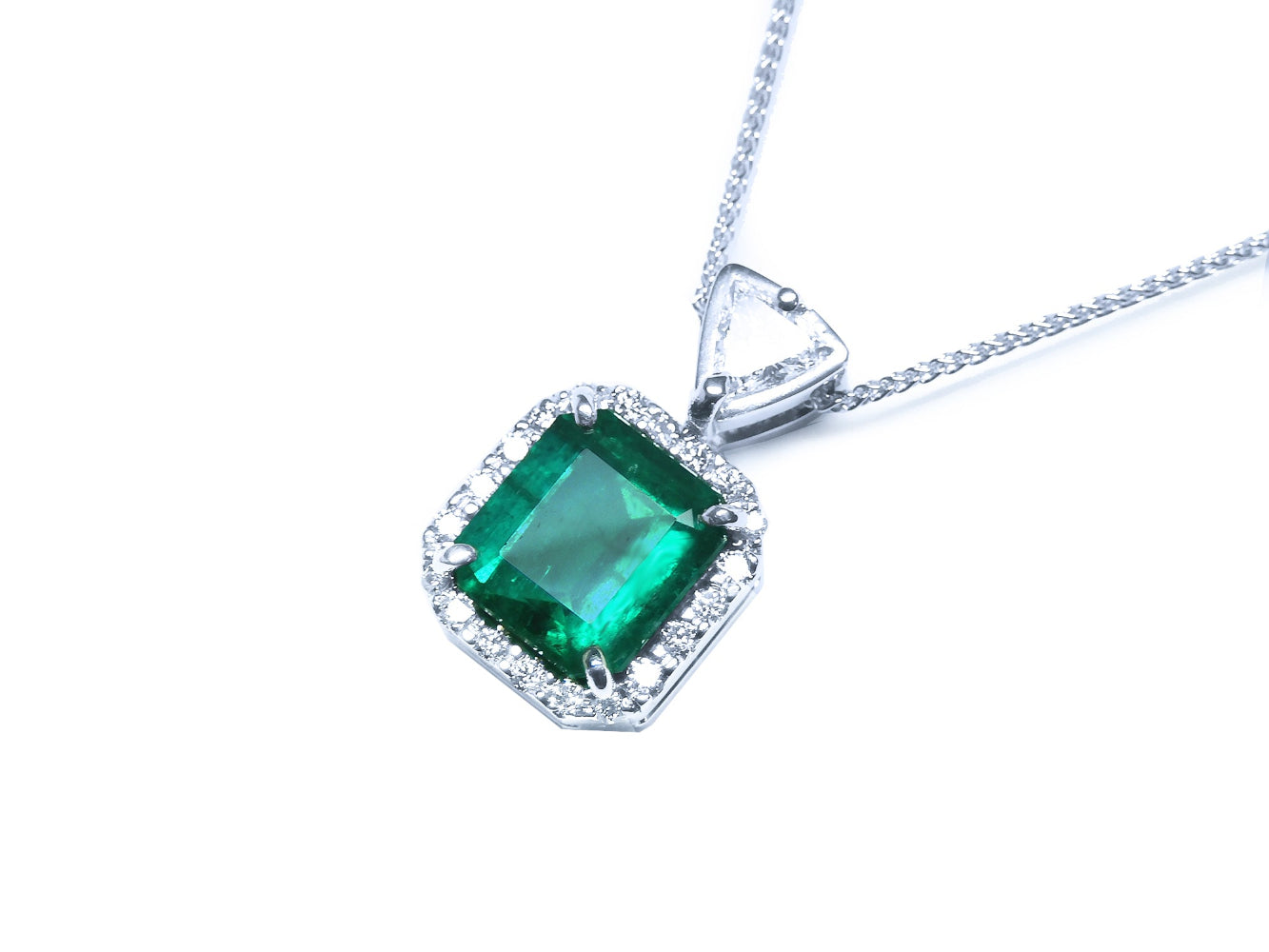 Displaying the topside this natural emerald pendant shows the halo diamond and the trillion-slider chain