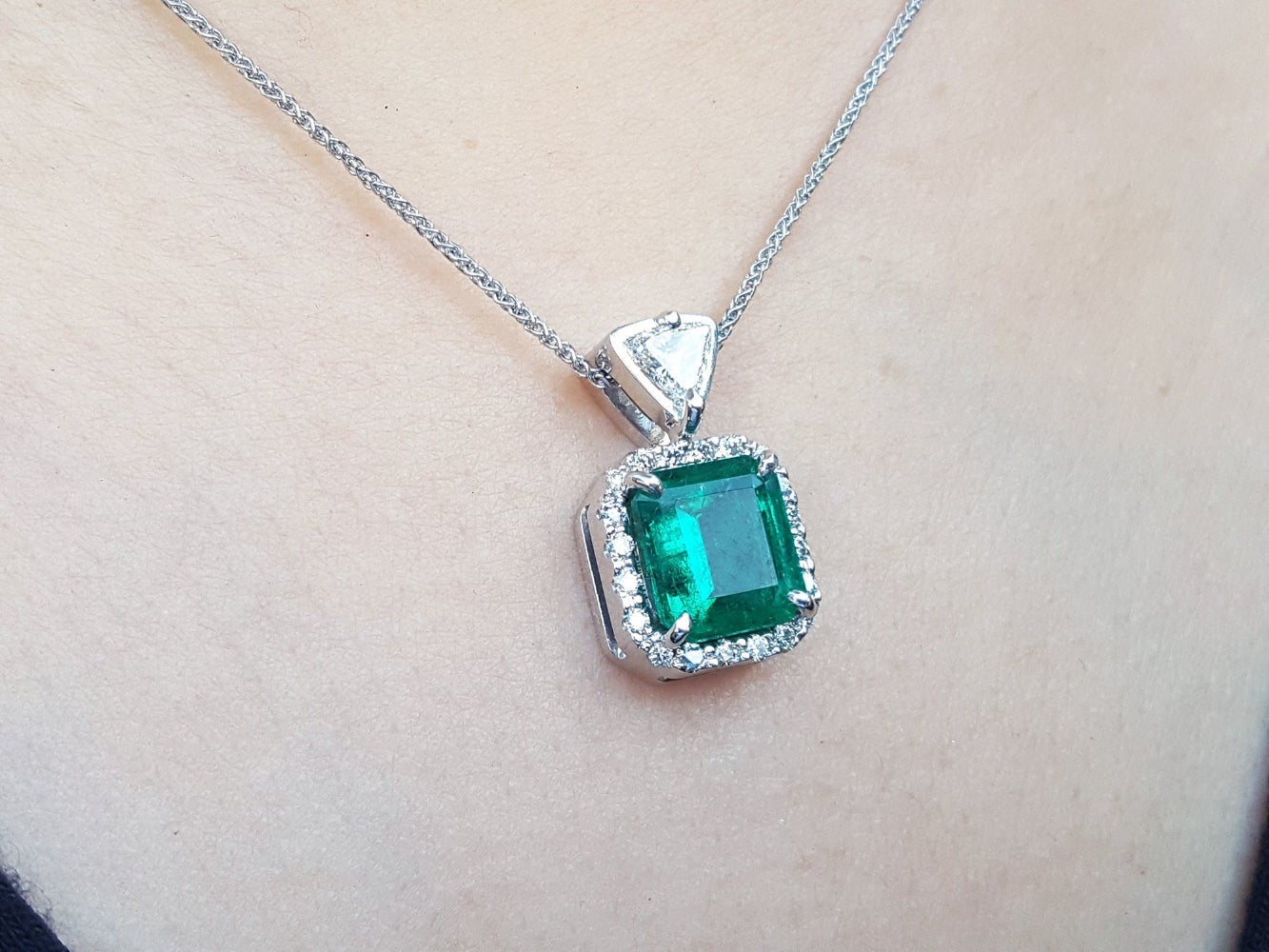 Emerald natural gemstone pendant on a gold chain against a neutral background.