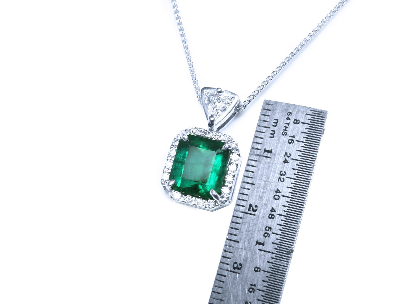 Emerald pendant on a white gold  chain with a ruler for scale on a white background.