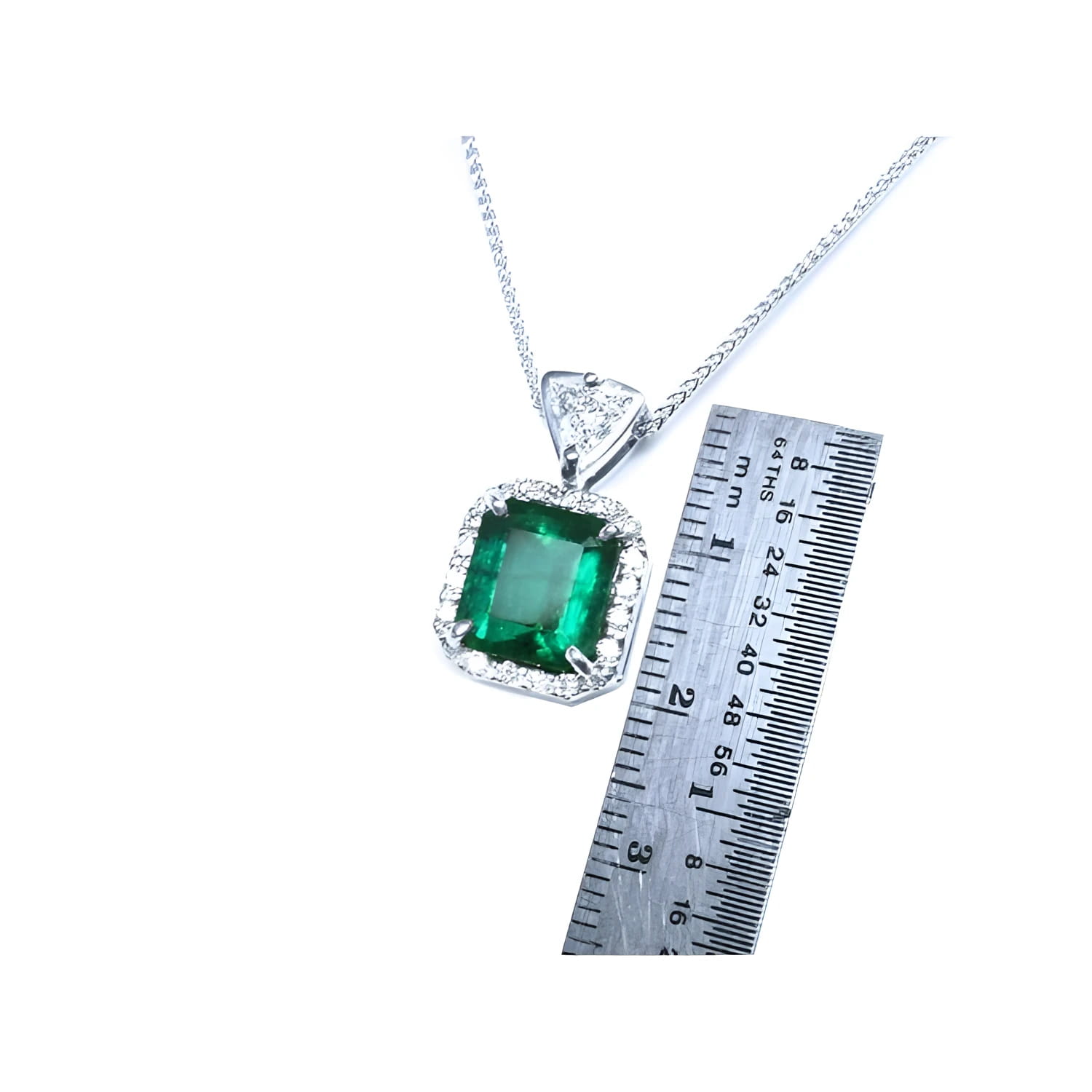 Emerald cut Colombian emerald pendant in 18K white gold with diamond halo, next to a ruler.