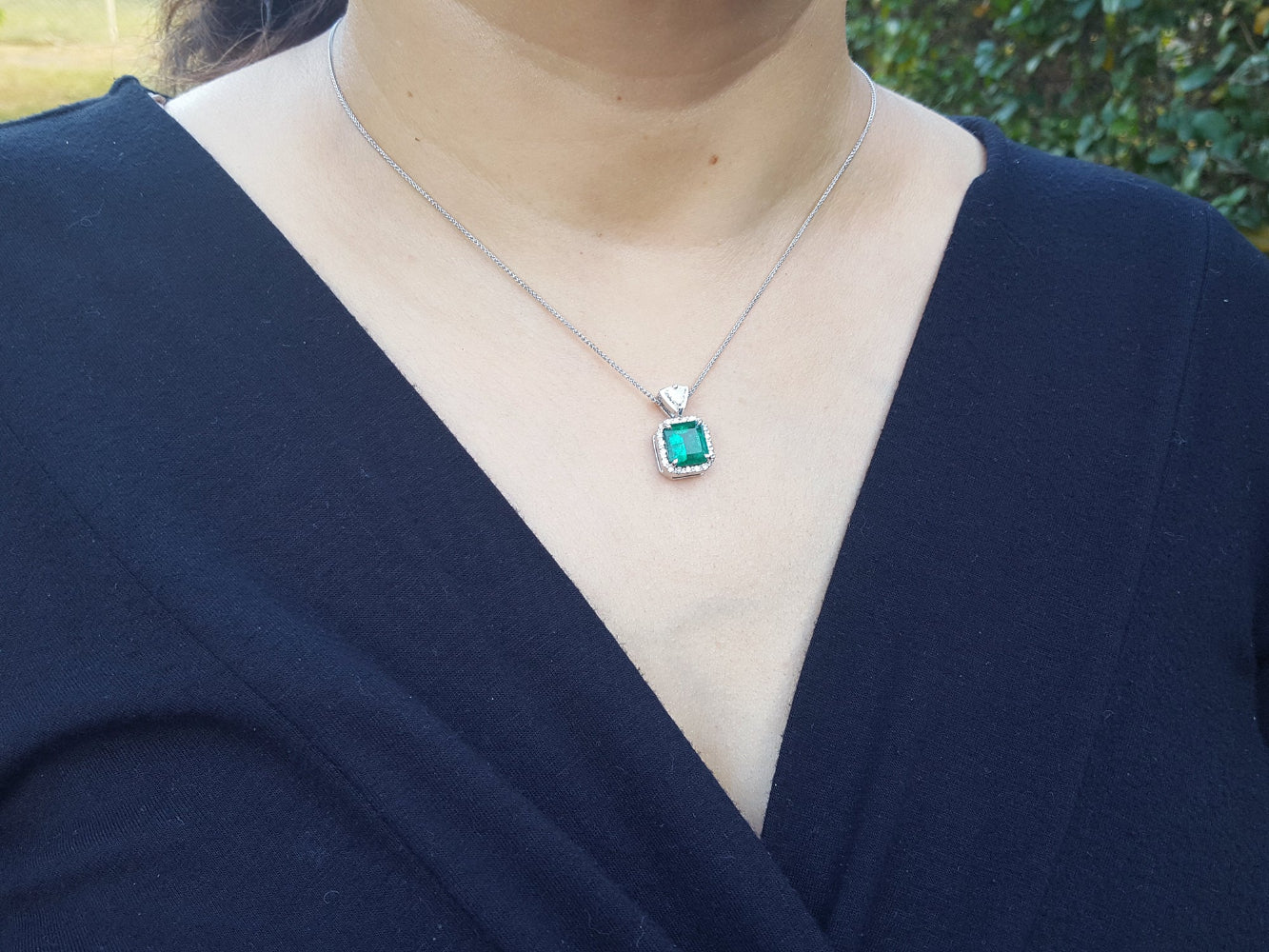 Person wearing a necklace with a colombian emerald pendant against a blurred natural background.