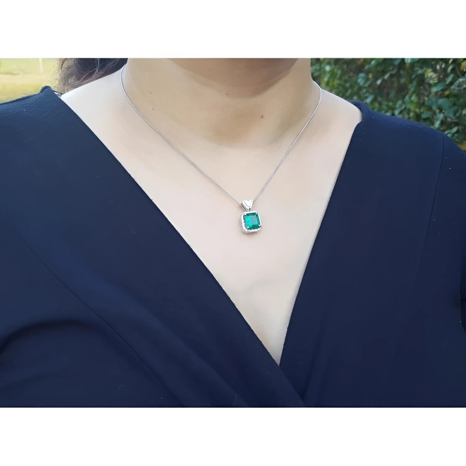 Colombian emerald pendant in 18K white gold, worn on a woman's neck.