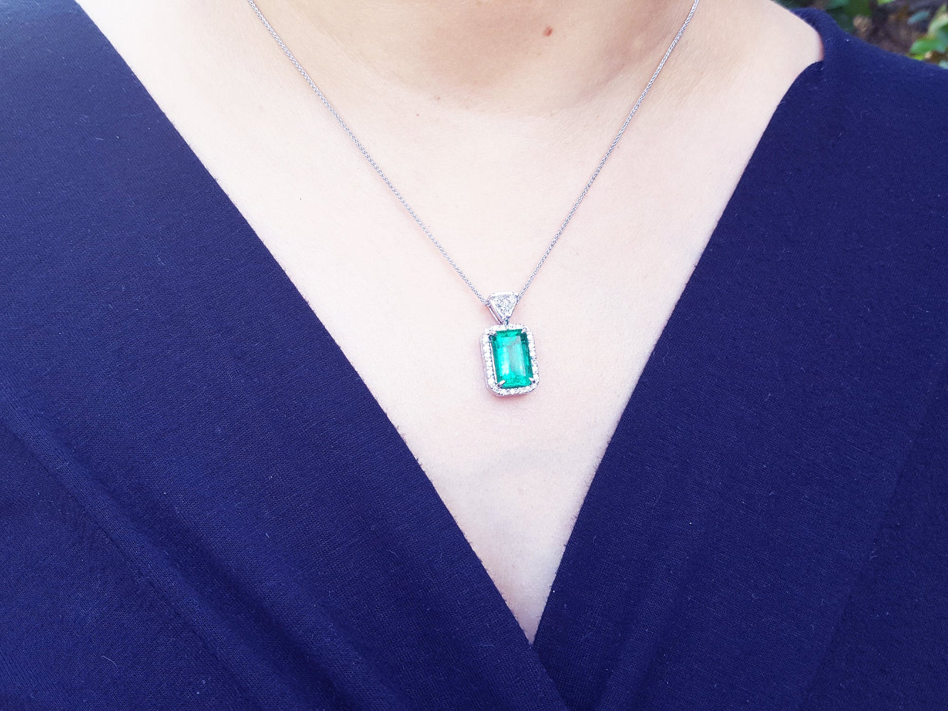 Person wearing a necklace with an emerald pendant against a dark blue background