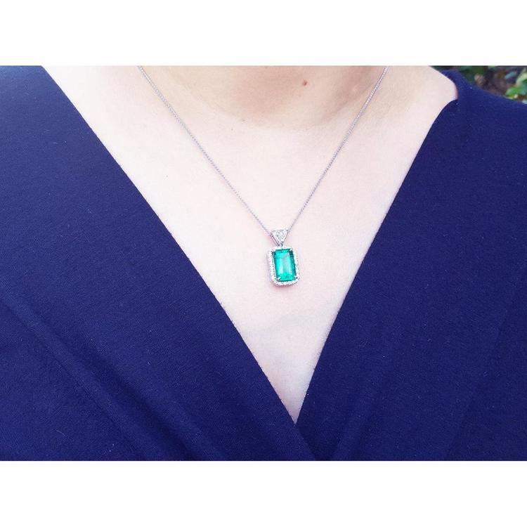 Person wearing a necklace with an emerald pendant against a dark blue background
