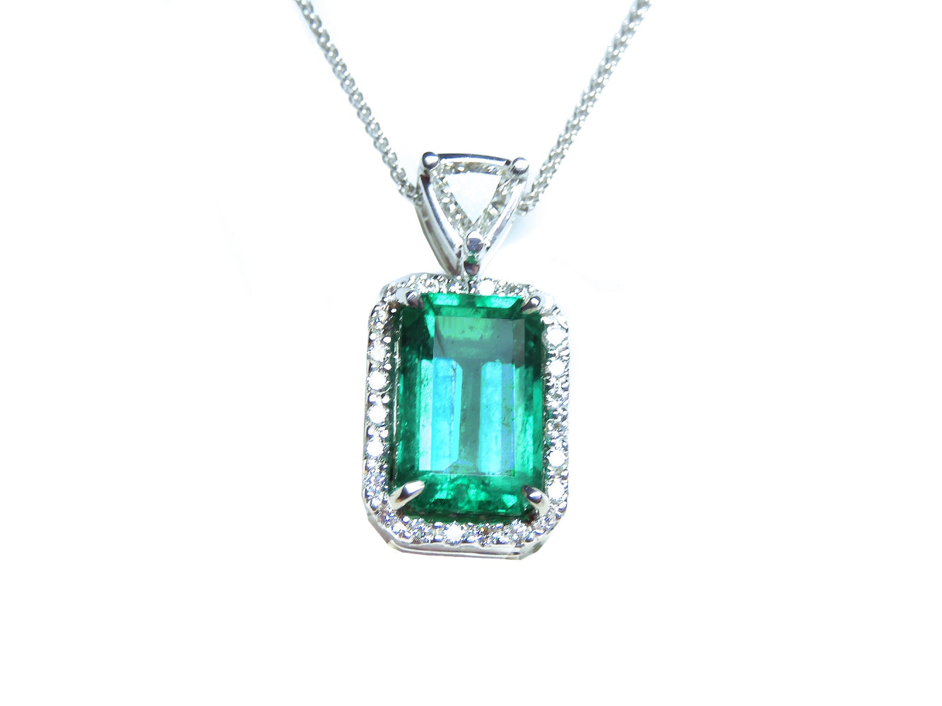 The topside of this certified natural emerald pendant shows the top bail slider with a trillion-cut diamond and the emerald with a halo diamond.