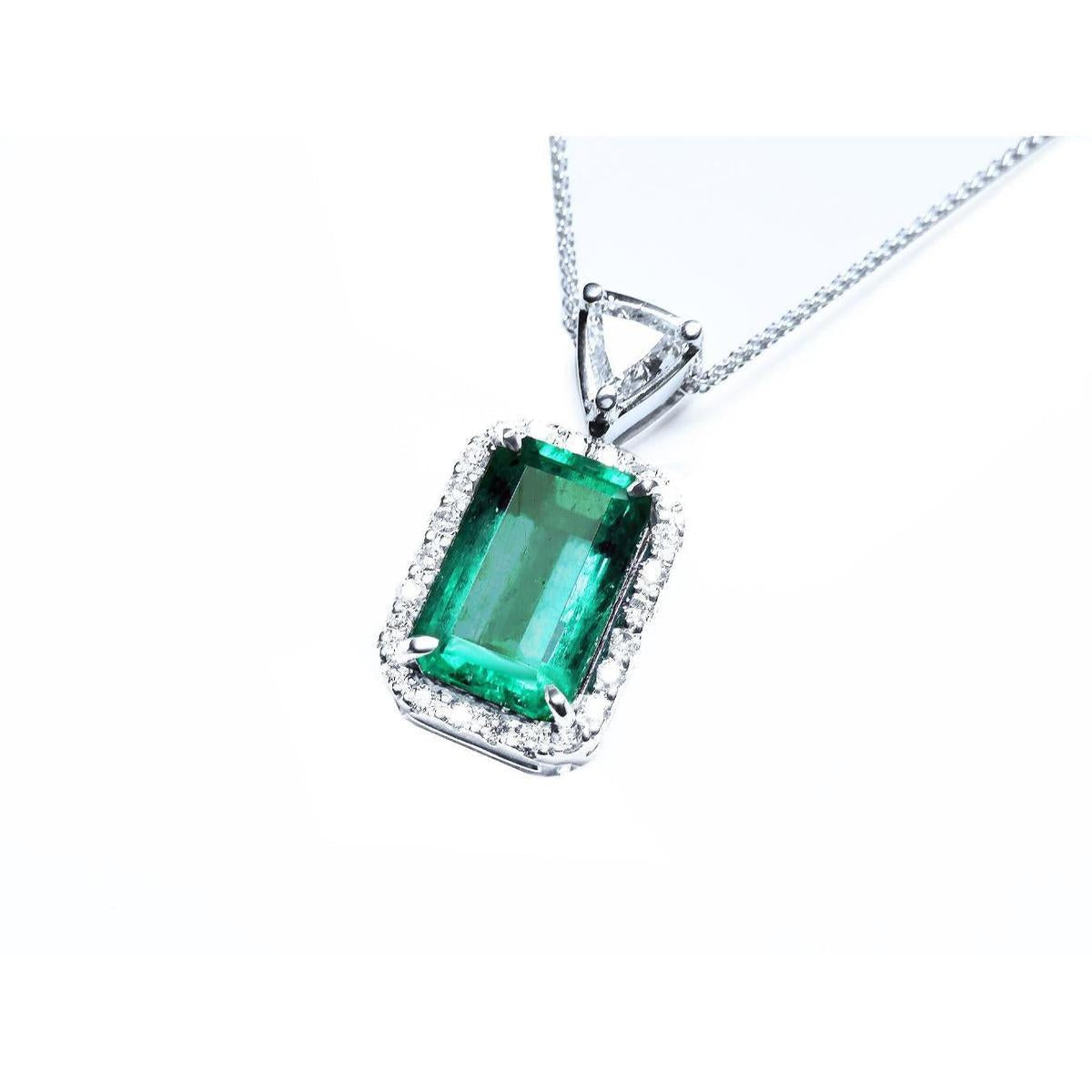 A rectangular emerald encircled by a halo diamond pendant with a top bail with trillion-cut diamond in white gold.
