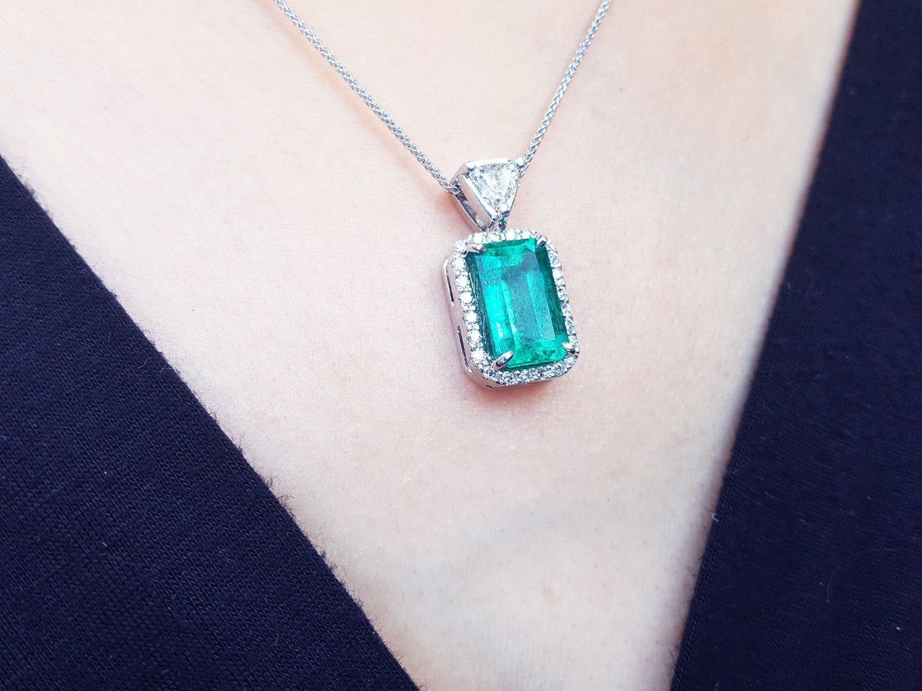 Emerald green gemstone pendant on a white gold chain against a dark background.