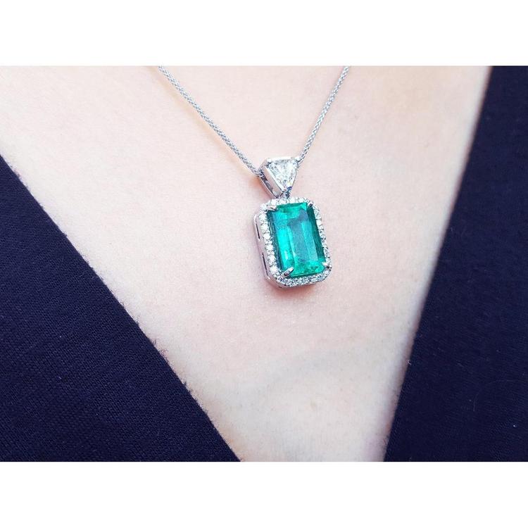 Emerald green gemstone pendant on a white gold chain against a dark background.