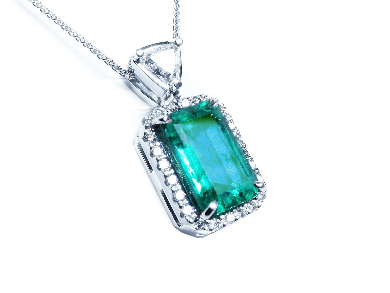 This GIA certified colombian emerald in this pendant is surrounded by a halo diamond, on the top bail a trillion-cut diamond.