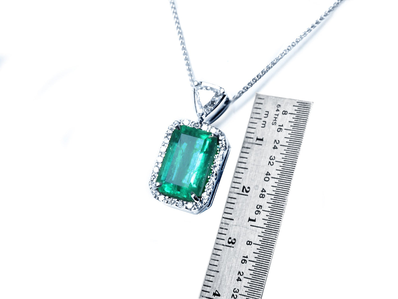 Emerald pendant on a chain with a ruler for scale on a white background