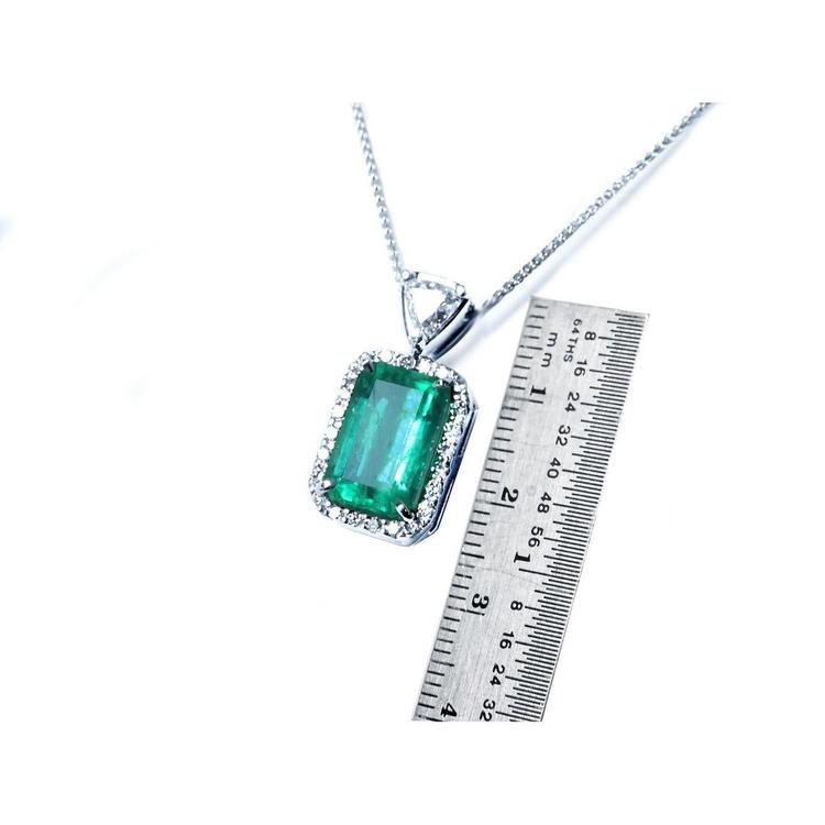 Emerald pendant on a chain with a ruler for scale on a white background