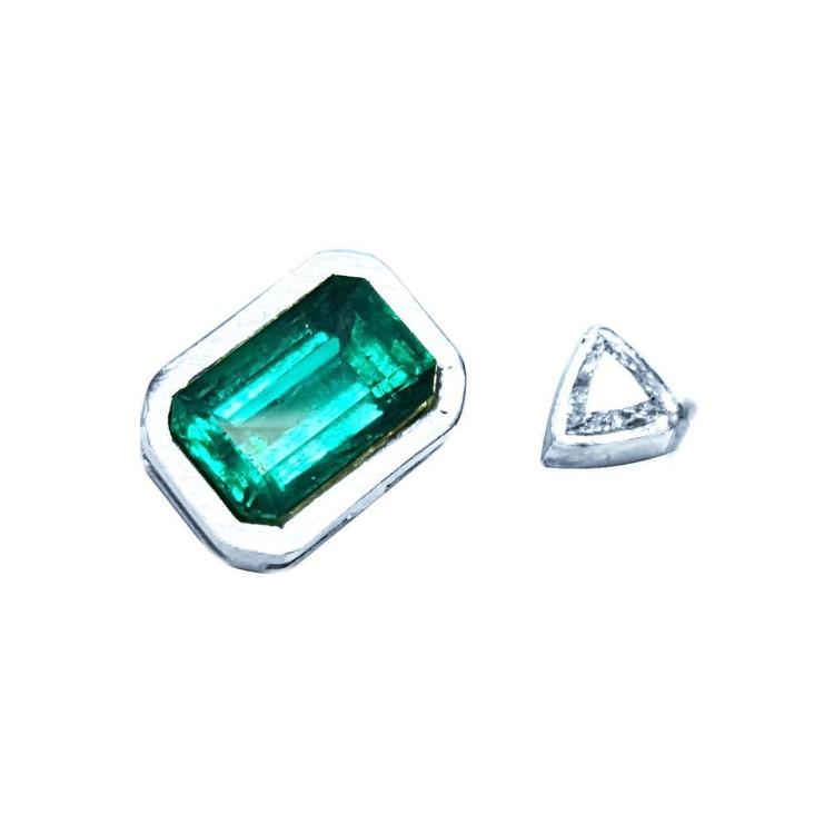 Green emerald and clear diamond on a white background showing the handcrafted setting on the rough.