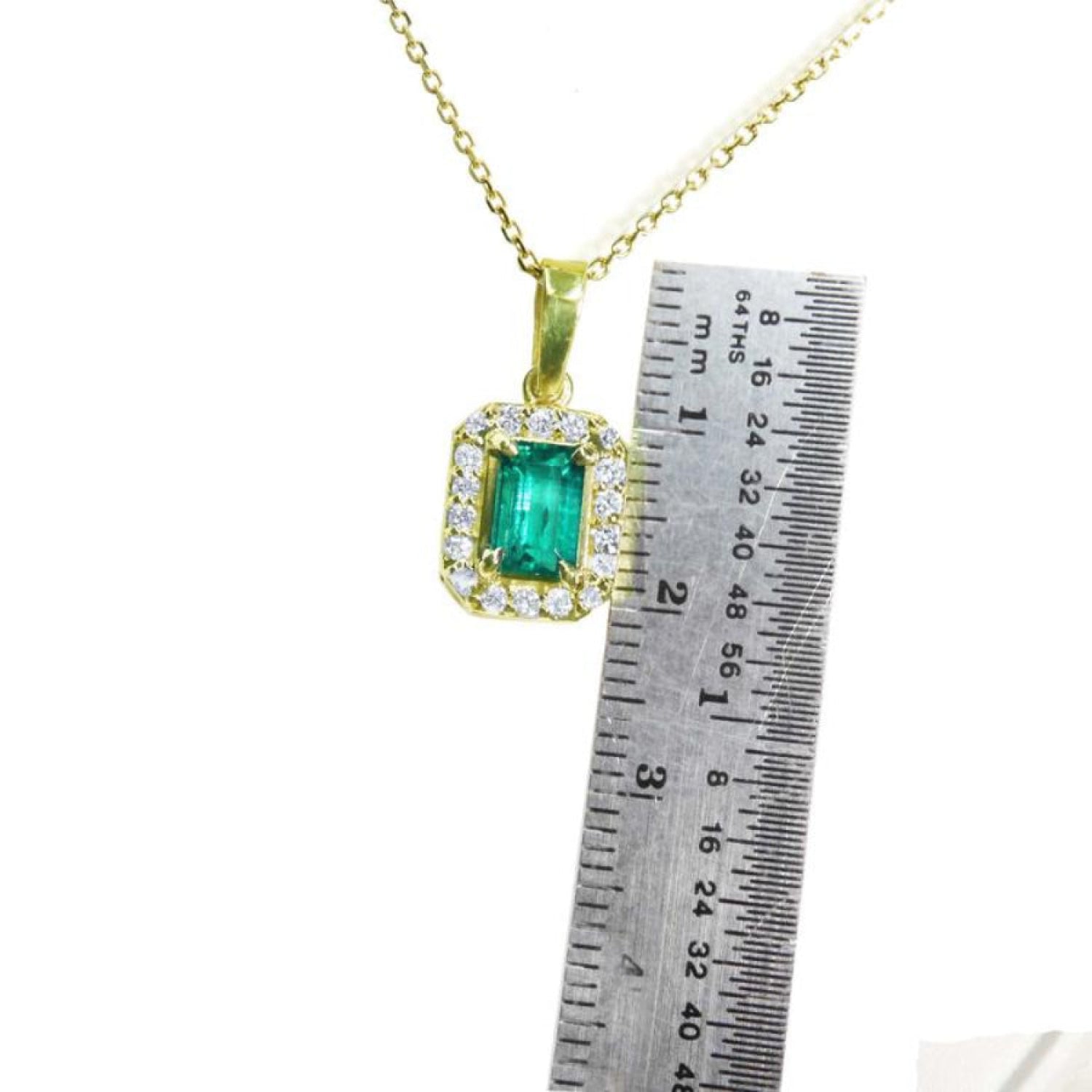 0.75 ct. GIA certified F1 Colombian emerald pendant in 18k yellow gold with diamond halo, next to a ruler.