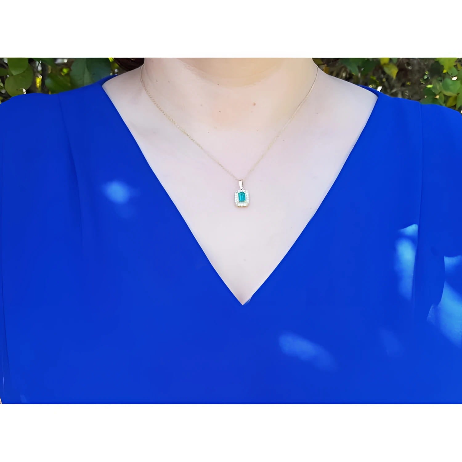 0.75 ct GIA F1 Colombian emerald pendant with diamond halo on 18k yellow gold chain, worn on a blue top.