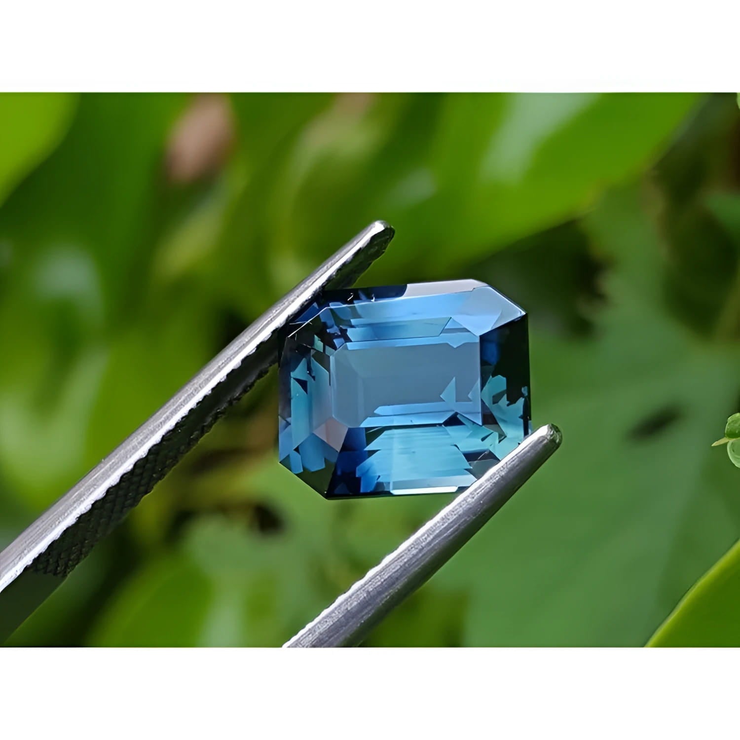 6.07 ct GIA certified rectangular emerald-cut natural untreated blue-green sapphire held by tweezers.