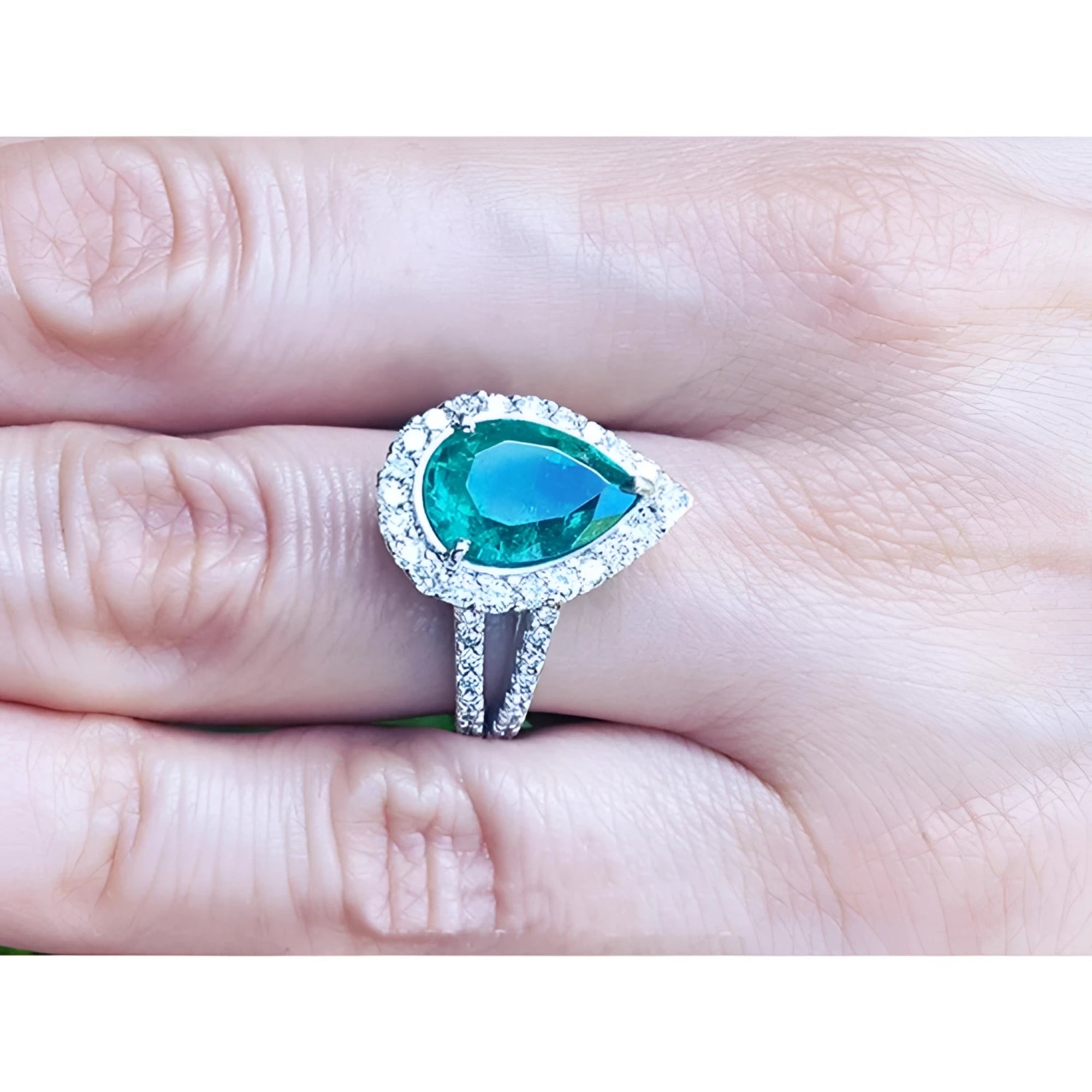 Brides' emerald engagement ring with a halo diamond crafted in white gold on a finger.