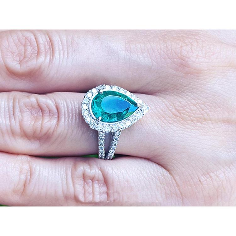 Brides' emerald engagement ring with a halo diamond crafted in white gold on a finger.