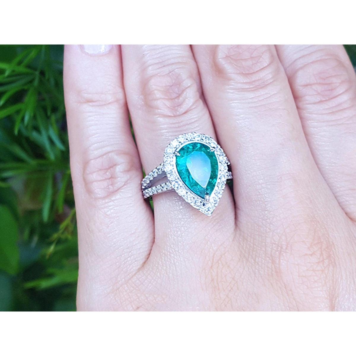 Ring with a teardrop emerald and halo diamond on a hand against a blurred green background.