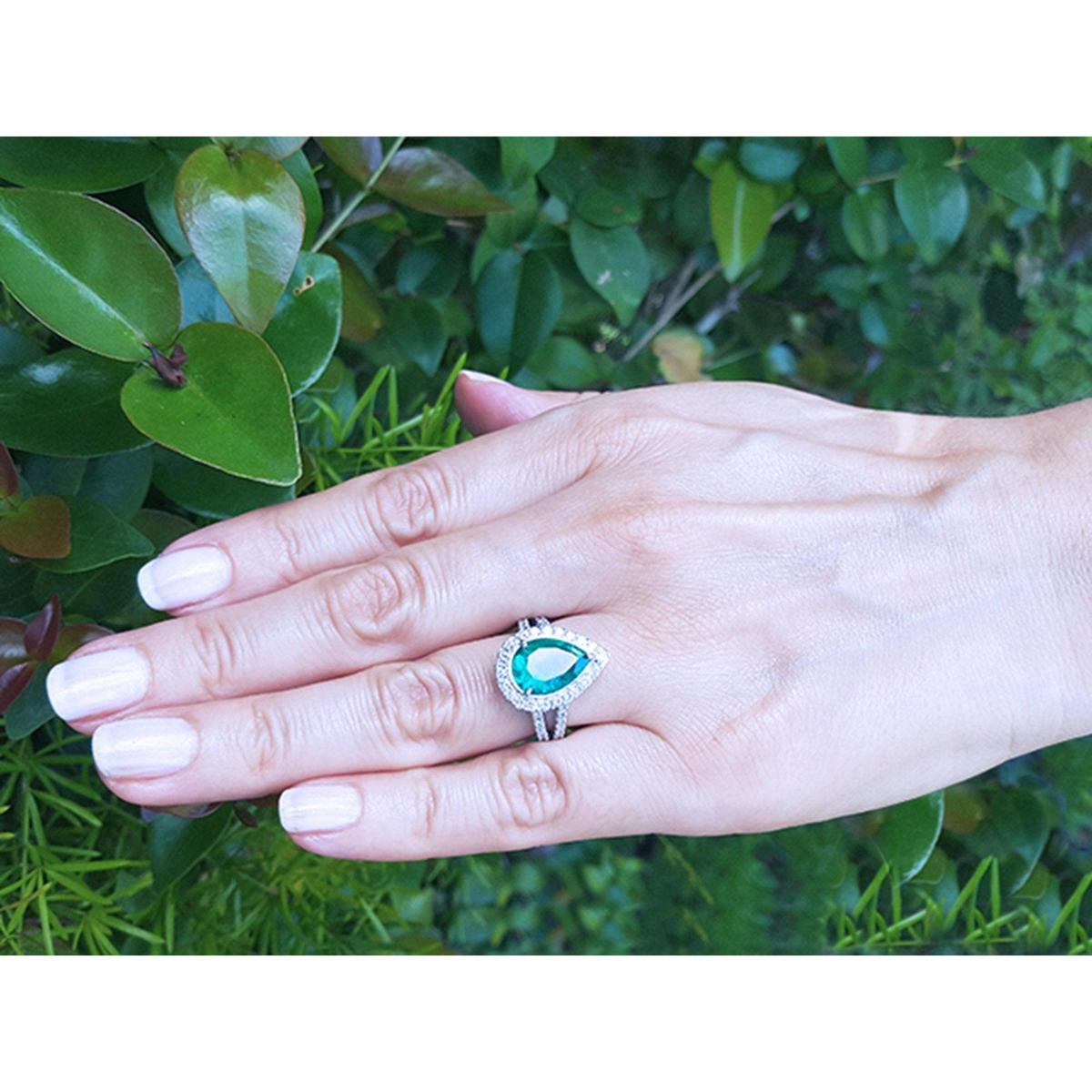 Hand wearing a Ladies' engagement ring with emerald pear cut, against a green leafy background.