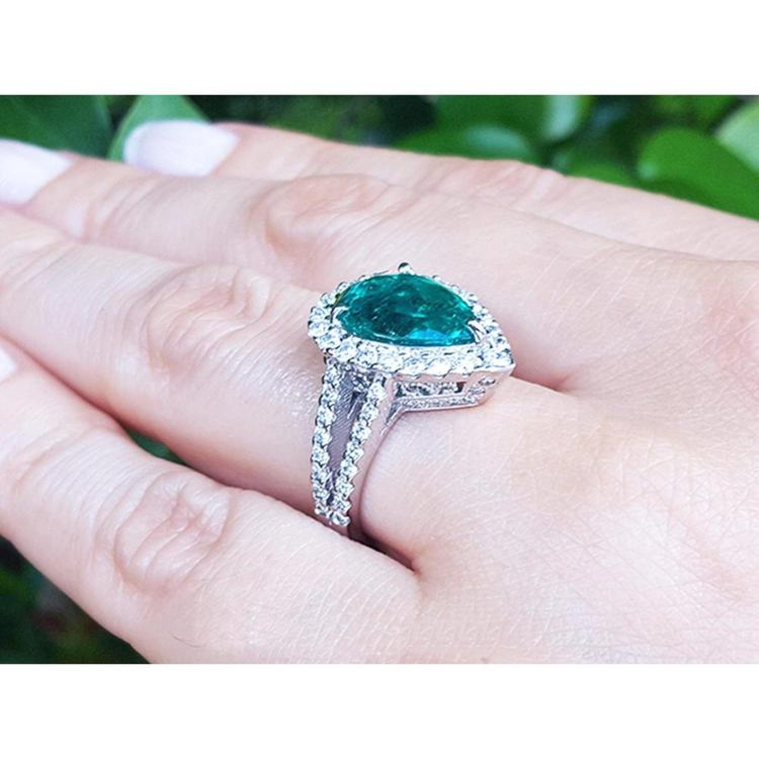 18K white gold ring with a 4.02 ct pear-shaped emerald and natural diamond halo on a hand.