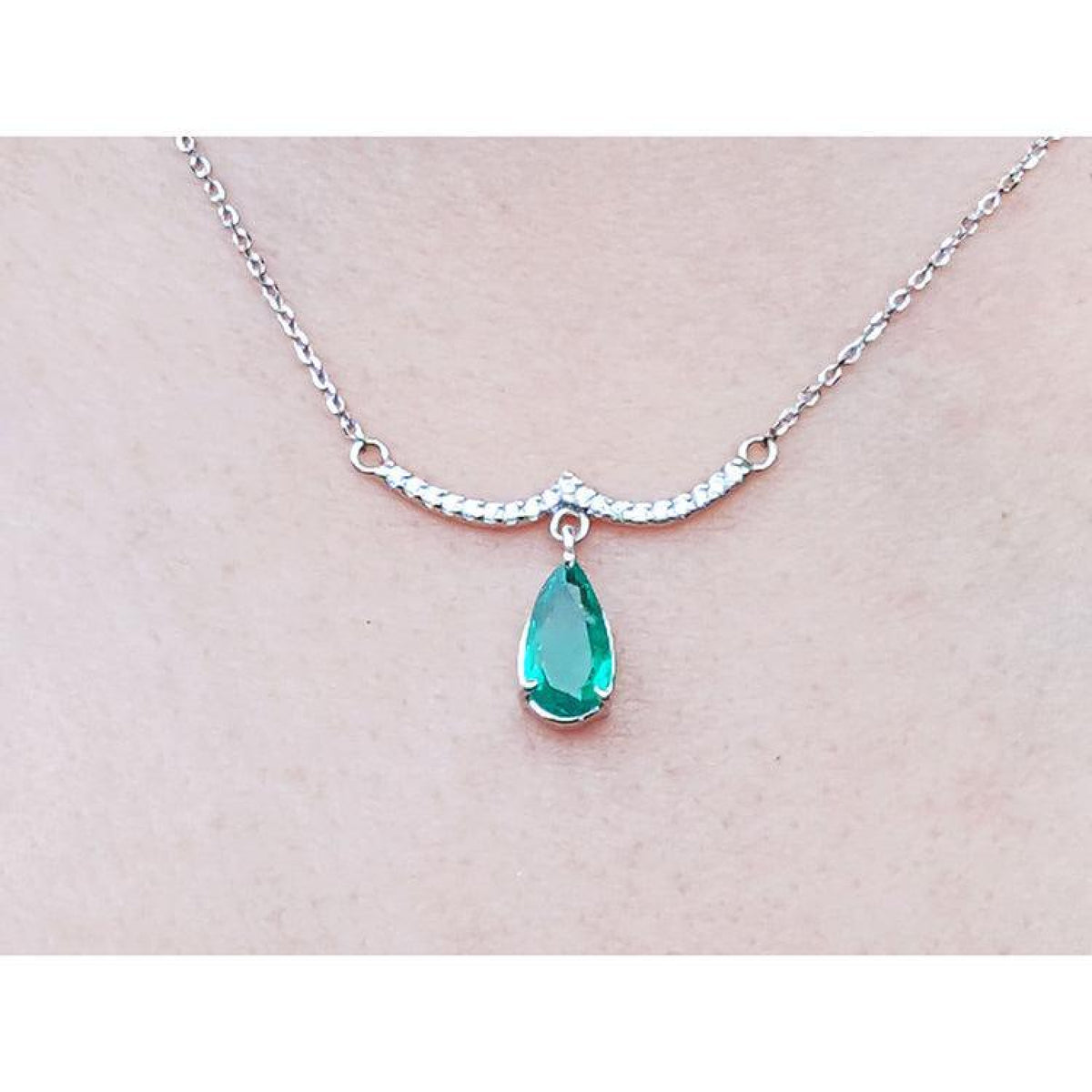 14K white gold necklace with a pear-shaped emerald dangling from a wavy diamond bar.