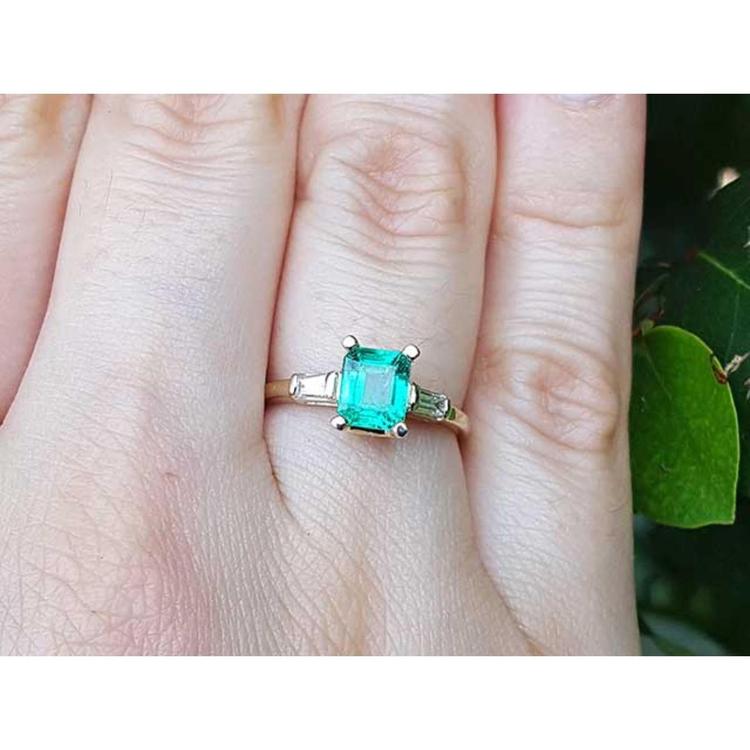 A 14k yellow gold natural Muzo colombian emerald ring with side diamonds on a person's finger.