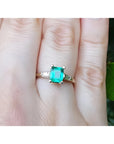 A 14k yellow gold natural Muzo colombian emerald ring with side diamonds on a person's finger.