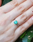 Hand wearing a, emerald May's birthstone ring against a leafy background.
