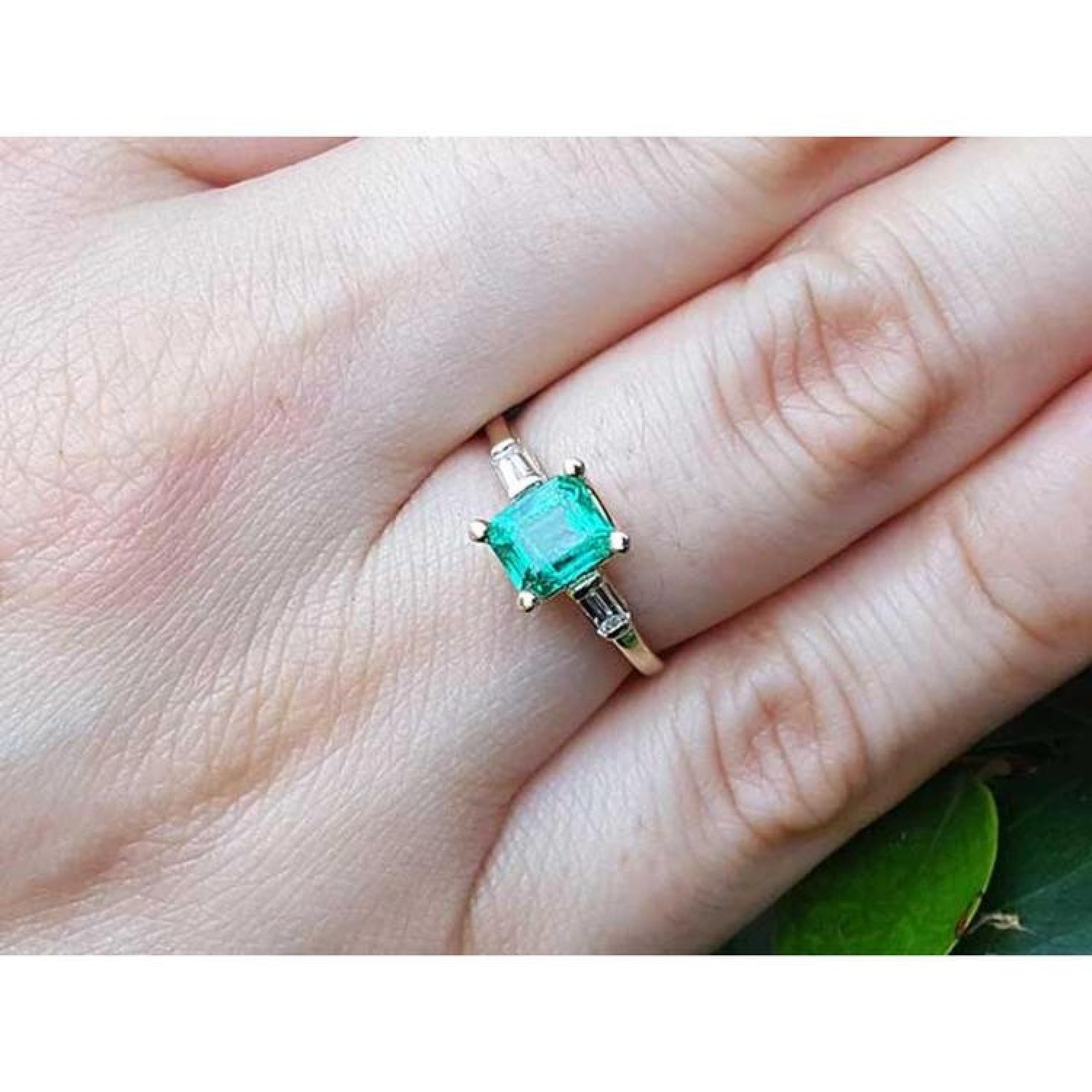14K yellow gold ring with a vibrant emerald and baguette side diamonds on a finger.