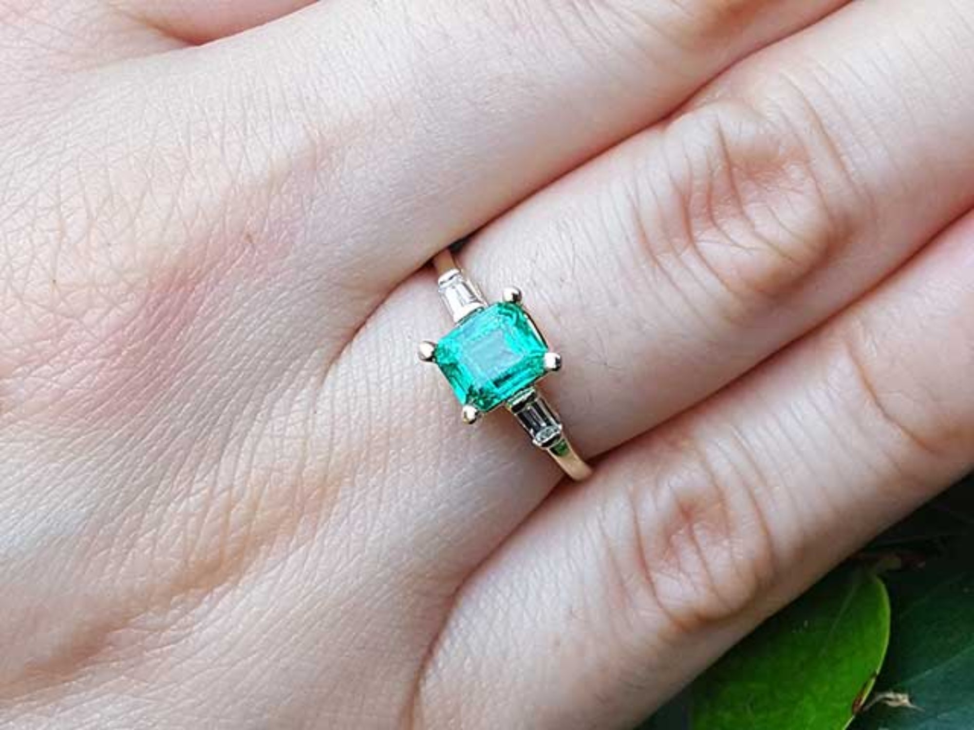 Emerald gemstone ring on a finger with a natural background.