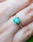 Emerald gemstone ring on a finger with a natural background.
