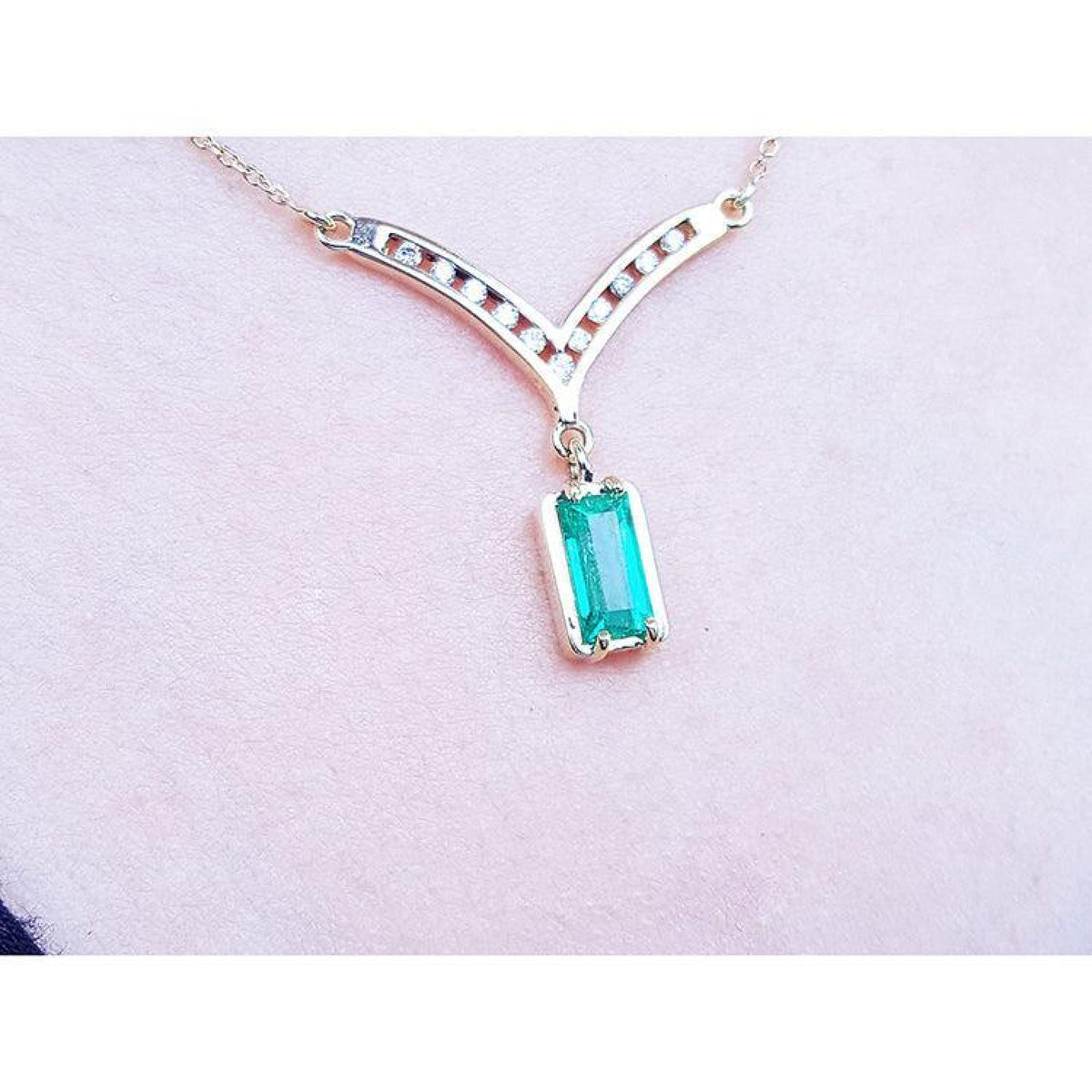 14K yellow gold necklace with a baguette-cut Colombian emerald pendant and diamond-studded V-shaped centerpiece.