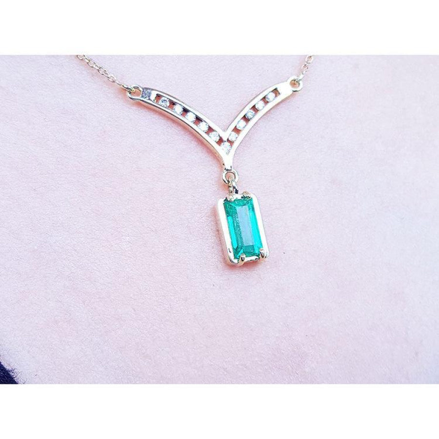 14K yellow gold necklace with a baguette-cut Colombian emerald pendant and diamond-studded V-shaped centerpiece.